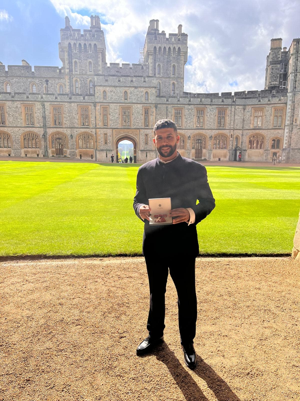 Ayoub, the refuge manager, standing on the grass at Windsor Castle in a dark suit, holding the medal box, with the castle behind him